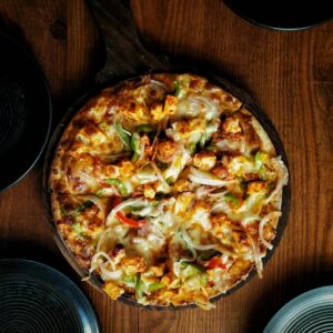 Mouthwatering close-up of a spicy paneer tikka pizza on a wooden table.