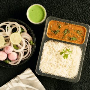 Delicious Indian meal featuring daal, white rice, onion salad, and green chutney from a top view perspective.