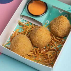 Three crispy croquettes with sauce on shredded fries, captured in a vibrant setting.