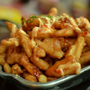 Delicious close-up of crispy french fries topped with cheese and sauce. Perfect for foodies.