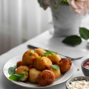 Crispy golden potato balls on a plate with fresh herbs, served with yummy dips.