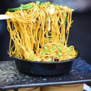 Tasty Indian street food featuring a bowl of stir-fried noodles with fresh vegetables.