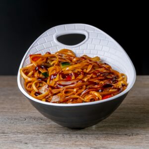 Close-up of savory stir-fried noodles with veggies in a unique black and white bowl.