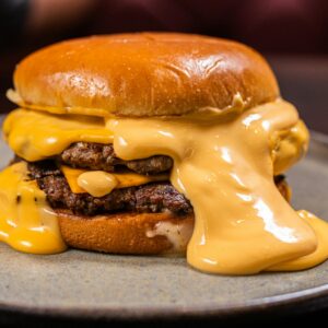 Close-up of a juicy burger with thick melted cheddar cheese, served on a plate.