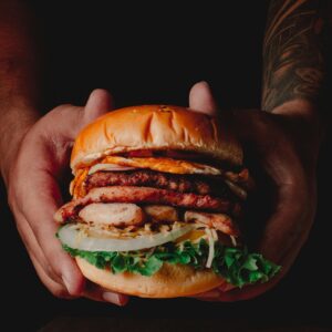 Close-up of a gourmet beef burger with fresh lettuce held by hands above a wooden board.