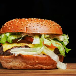 Close-up of a juicy cheeseburger with lettuce, tomato, and cheese in a sesame seed bun.