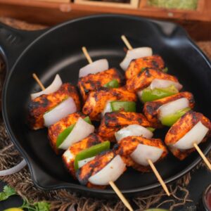 Close-up of grilled paneer skewers with bell peppers and onions on black plate.