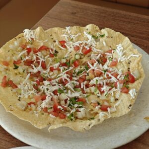 Close-up of a crispy masala papad topped with fresh tomato, onion, and cilantro.