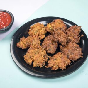 Delicious crispy pakoras served with tangy ketchup on a pastel backdrop.