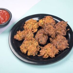 Delicious crispy pakoras served with tangy ketchup on a pastel backdrop.