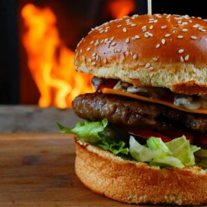 Delicious cheeseburger with fresh lettuce, tomatoes, and beef patty in front of a flaming backdrop.