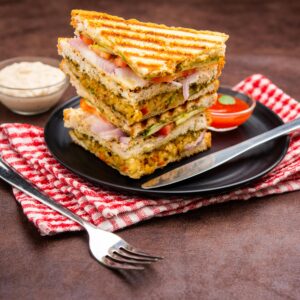 Delicious stacked vegetable grilled sandwiches on a plate with sauces and fork on a napkin.