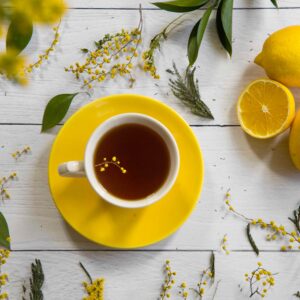 A vibrant flat lay of lemon tea with yellow flowers and citrus fruits on white.