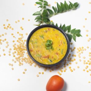Mouthwatering Indian yellow lentil soup garnished with herbs, served with tomatoes and curry leaves.
