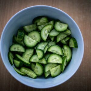 Top view of freshly chopped green cucumbers in a crisp white bowl on a wooden surface.
