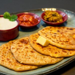 Appetizing Indian paratha served with yogurt and pickles on a blue plate.