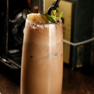 Refreshing chocolate milkshake topped with mint, served in a glass with a straw and spoon.