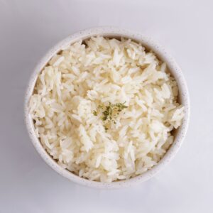 Close-up of cooked white rice in a bowl, garnished with herbs, in a minimalist setup.