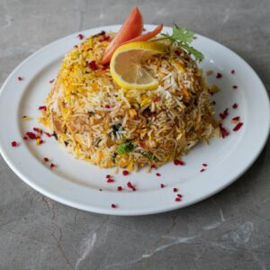A vibrant plate of biryani garnished with lemon and tomatoes on a marble surface.
